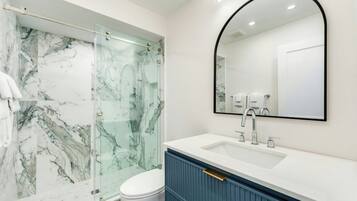 A bathroom with a glass shower enclosure, a white sink with a blue cabinet, and a large mirror.