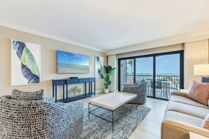 A modern living room with a sofa, a coffee table, and a TV. There is a balcony with a view of the ocean. - South Seas (Captiva)