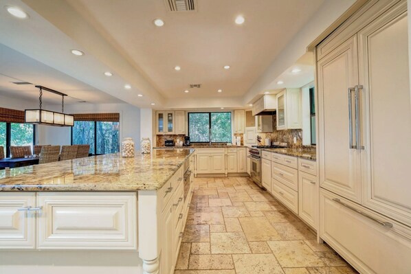 A spacious kitchen with a large island, white cabinetry, and a view through the windows. - South Seas (Captiva)