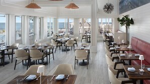 A restaurant with multiple tables and chairs, large windows with a view of the ocean, and hanging pendant lights. - South Seas (Captiva)