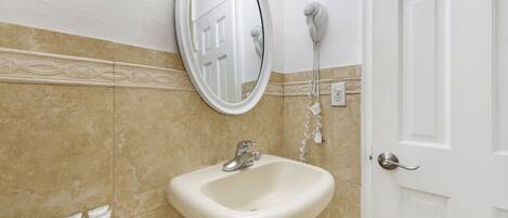 Un baño con lavamanos, espejo y secador de pelo.