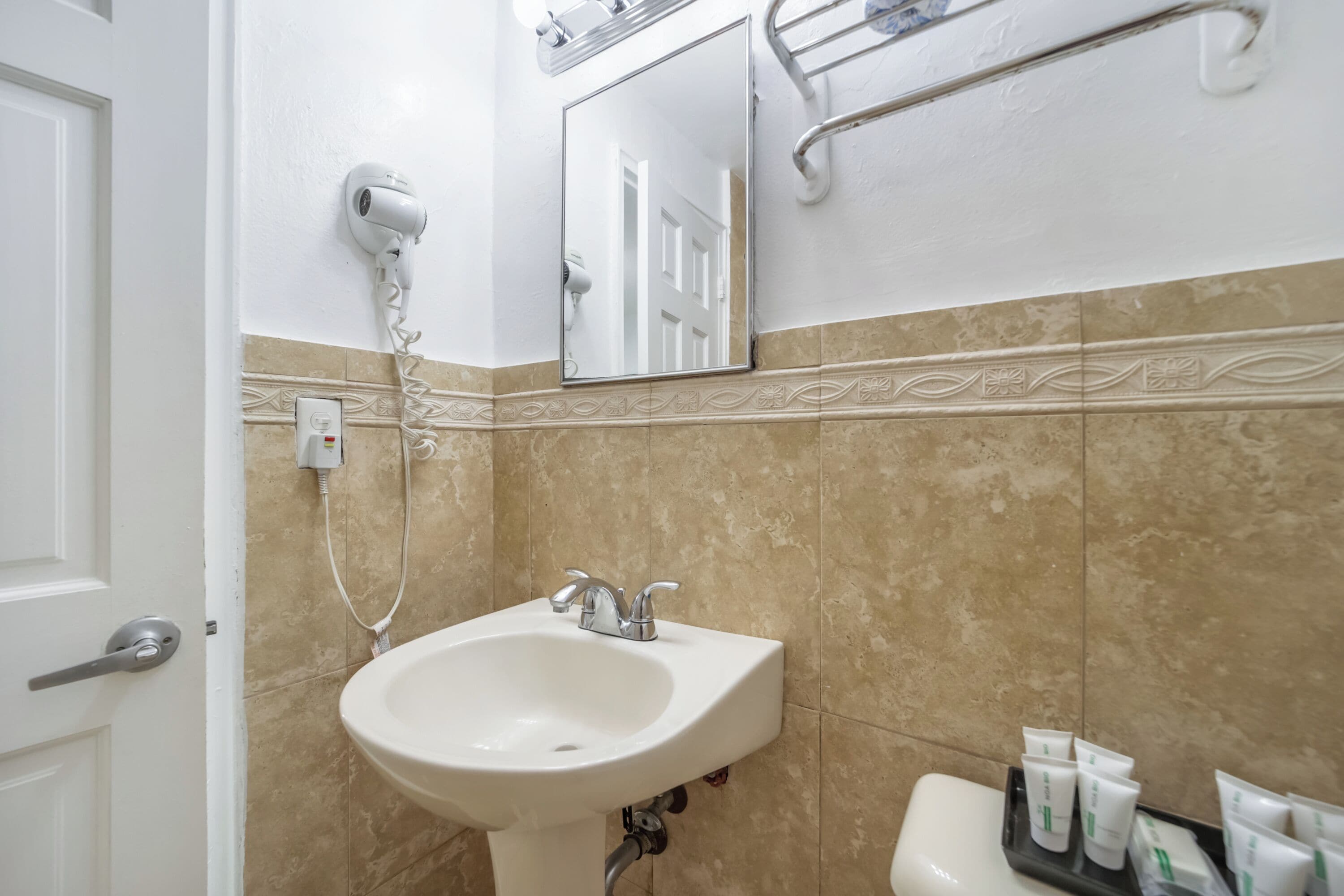 A bathroom with a white sink, a mirror, a hairdryer, and toiletries on a shelf.