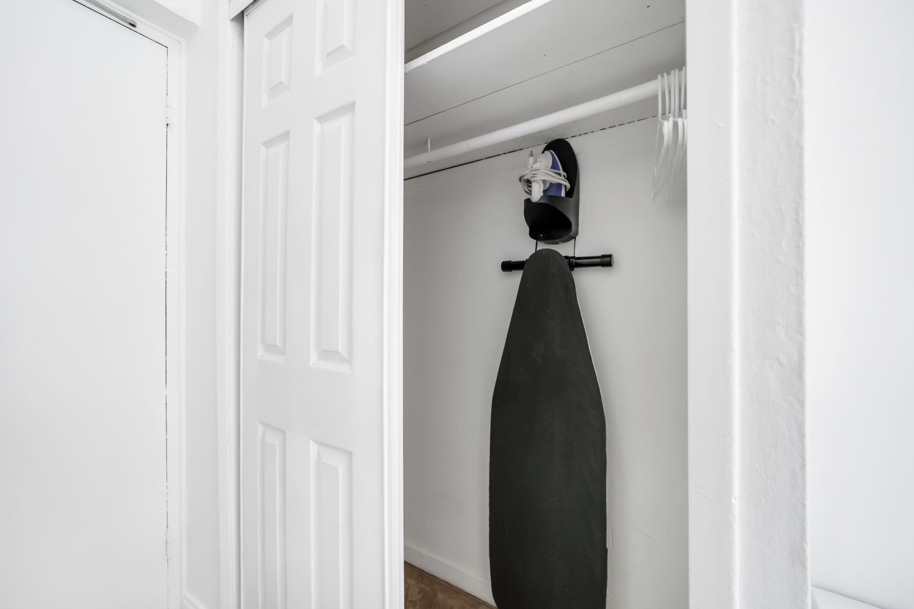 A white door with a black surfboard hanging on a rack in a hallway.