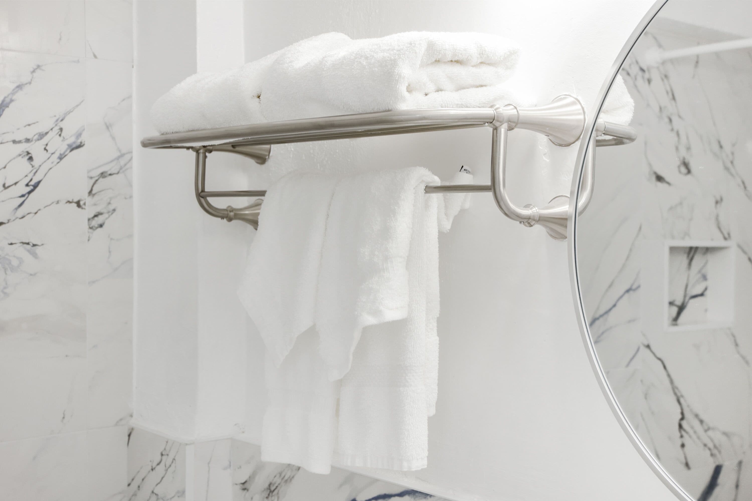 A bathroom with a marble wall, a towel rack with folded towels, and a mirror reflecting the wall.