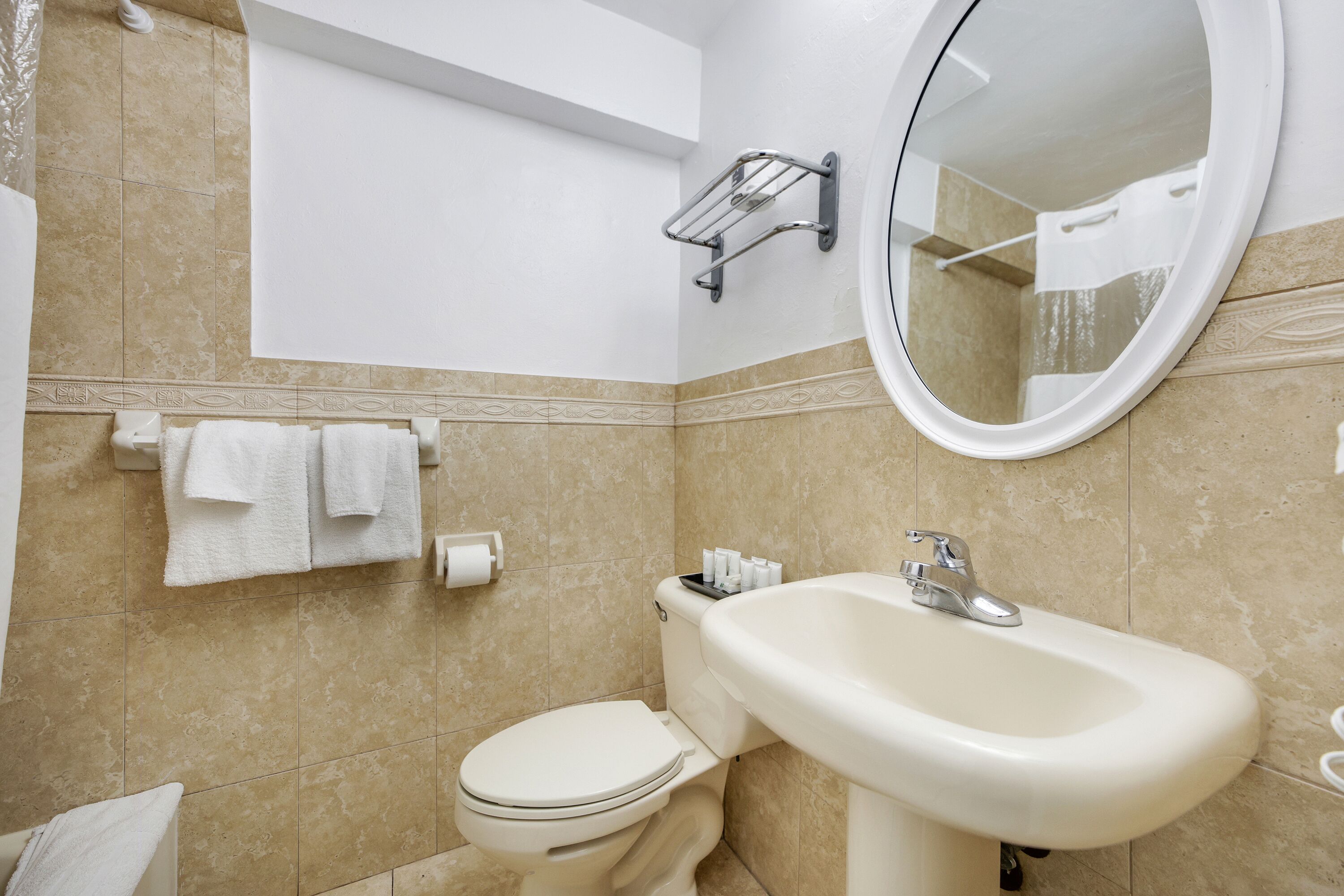 A bathroom with a toilet, sink, mirror, towel rack, and toiletries.