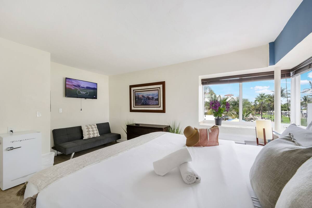 Una camera d'albergo con un letto, una televisione, un divano, una scrivania e una finestra vista.