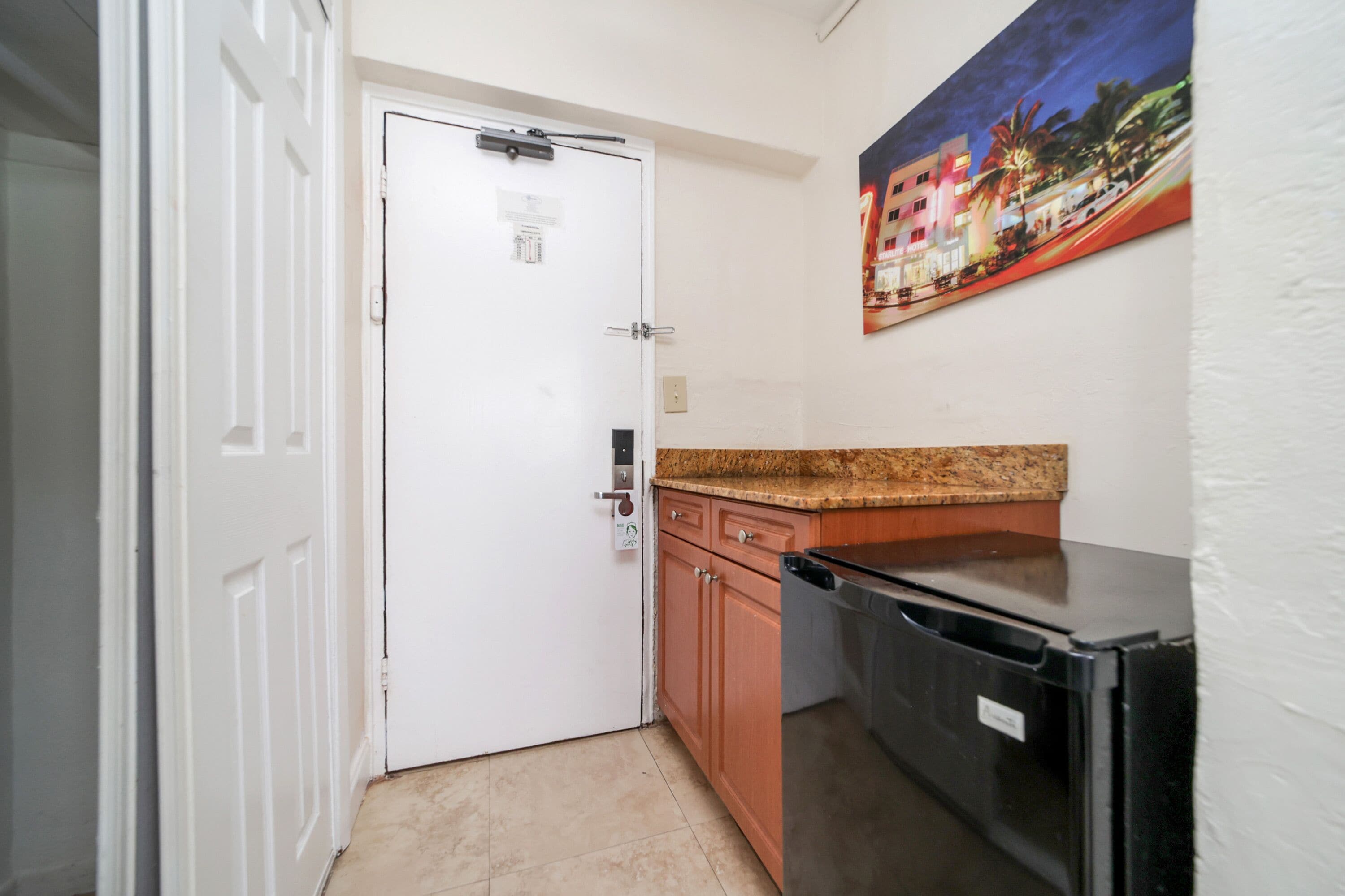A compact kitchen with a white door, wooden cabinets, a granite countertop, and a black refrigerator.