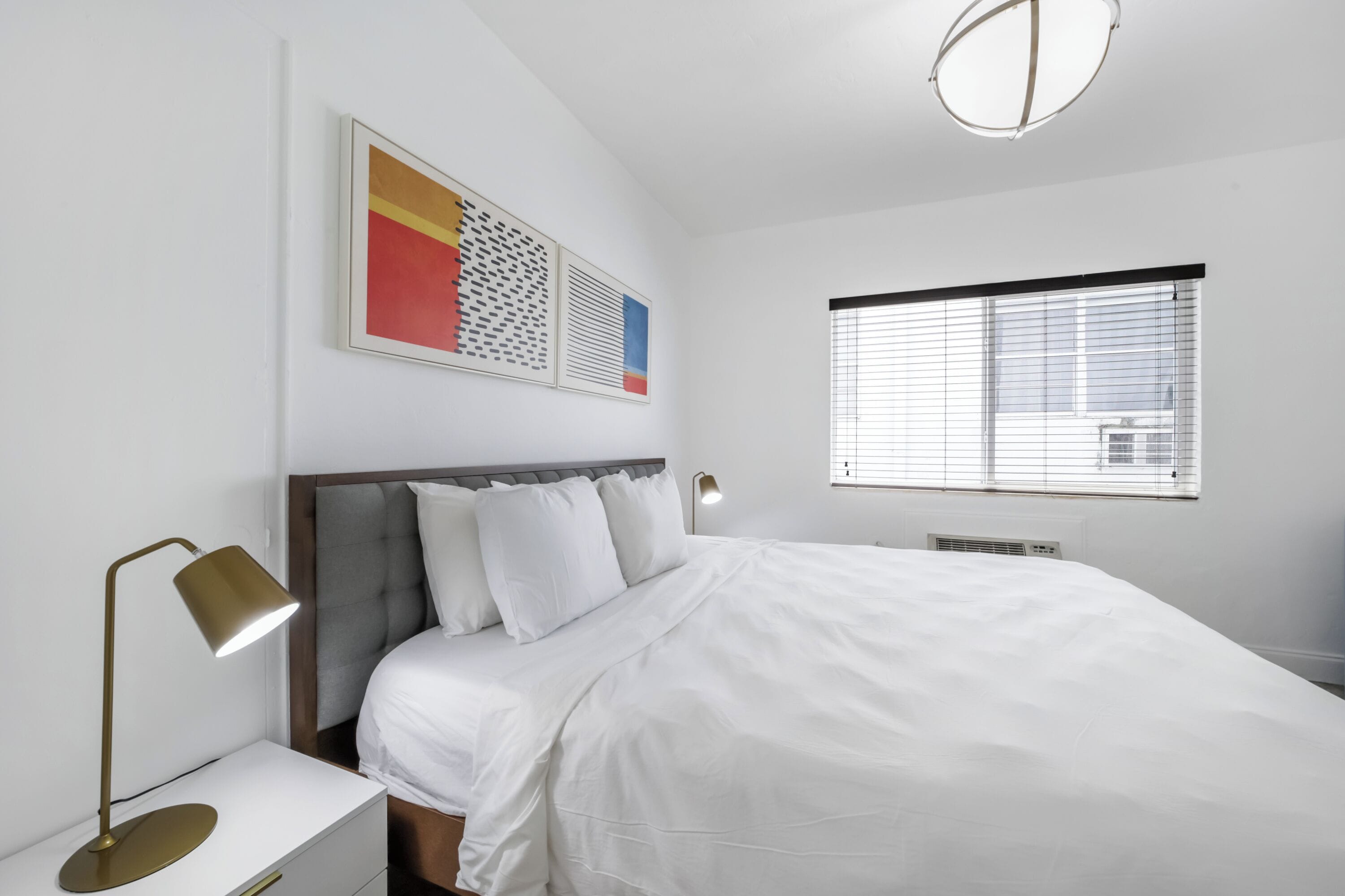 A neatly made bed with white bedding, a bedside lamp, and a wall-mounted artwork.