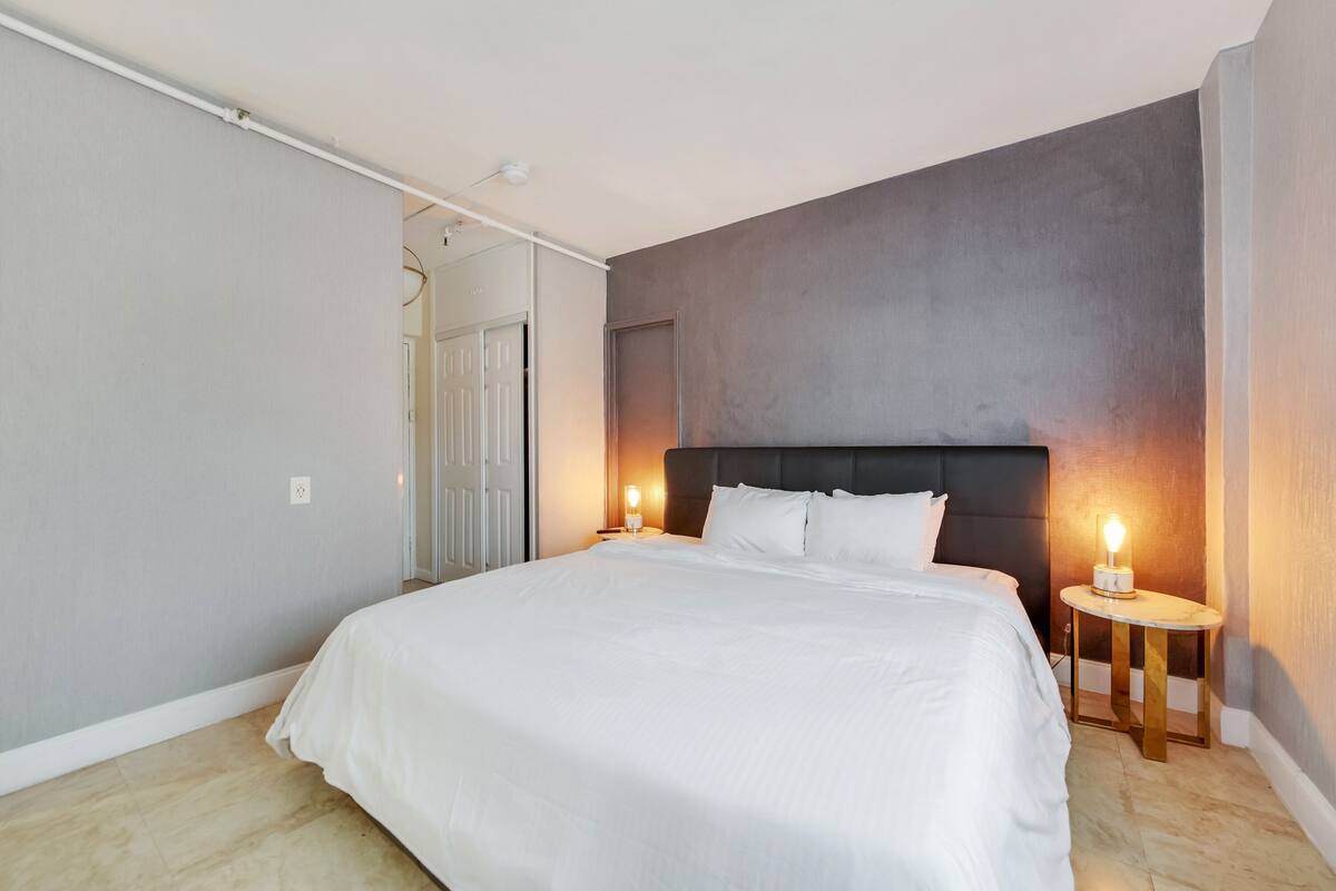 Una camera da letto con un letto grande, due comodini, una testiera e una porta che dà su un'altra stanza.