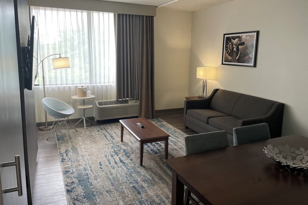 A hotel room with a sofa, a dining table, a chair, a lamp, and a picture on the wall.