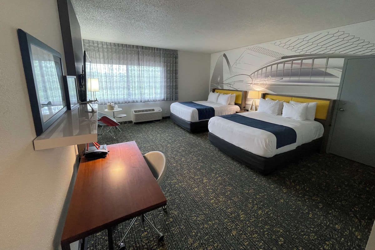 A hotel room with two beds, a desk, a chair, and a large window with curtains.