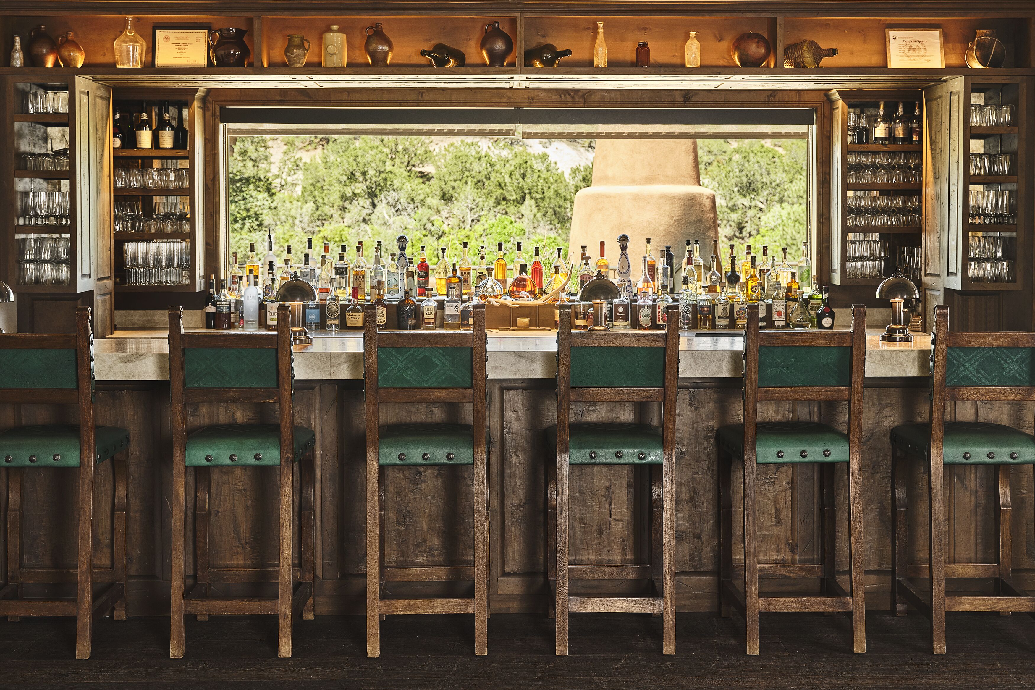 A bar with wooden chairs and a variety of bottles and glasses.