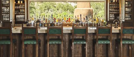 A bar with wooden chairs and a variety of bottles and glasses.