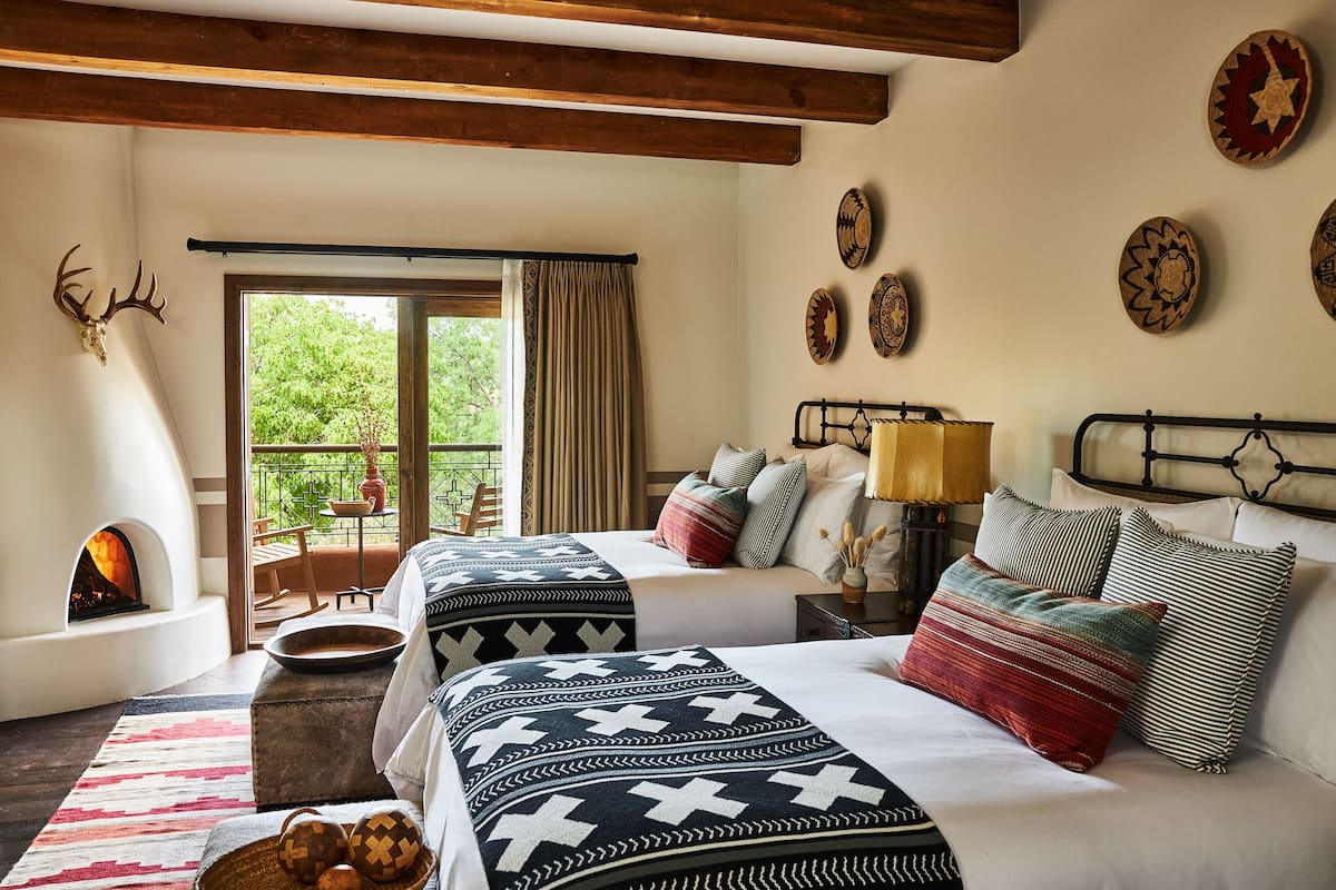A cozy bedroom with two beds, a fireplace, and a balcony with a view of greenery.