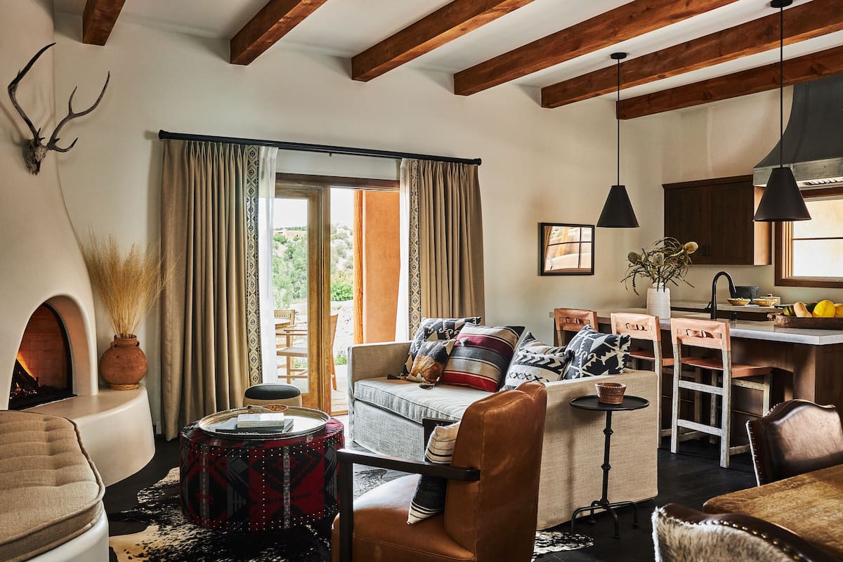A cozy living room with a fireplace, a sofa, a coffee table, and a dining area with chairs and a kitchen counter.