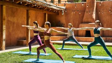Un grupo de personas practicando yoga sobre colchonetas en un entorno exterior, con un edificio rústico al fondo.