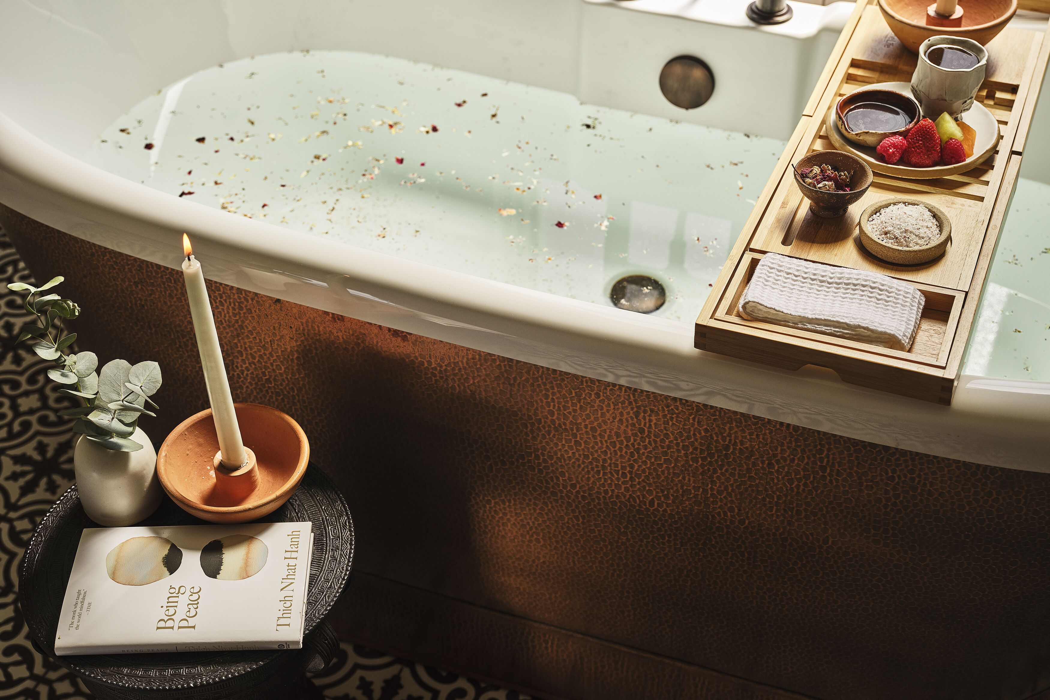 Una bañera con una bandeja de productos de baño y un libro titulado 'Being Peace' de Thich Nhat Hanh.
