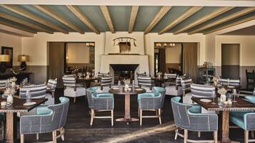 A dining area with multiple round tables, upholstered chairs, and a fireplace.