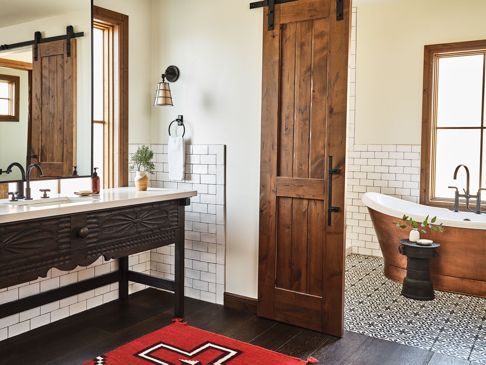 A bathroom with a wooden door, a white sink, a large mirror, and a freestanding bathtub.