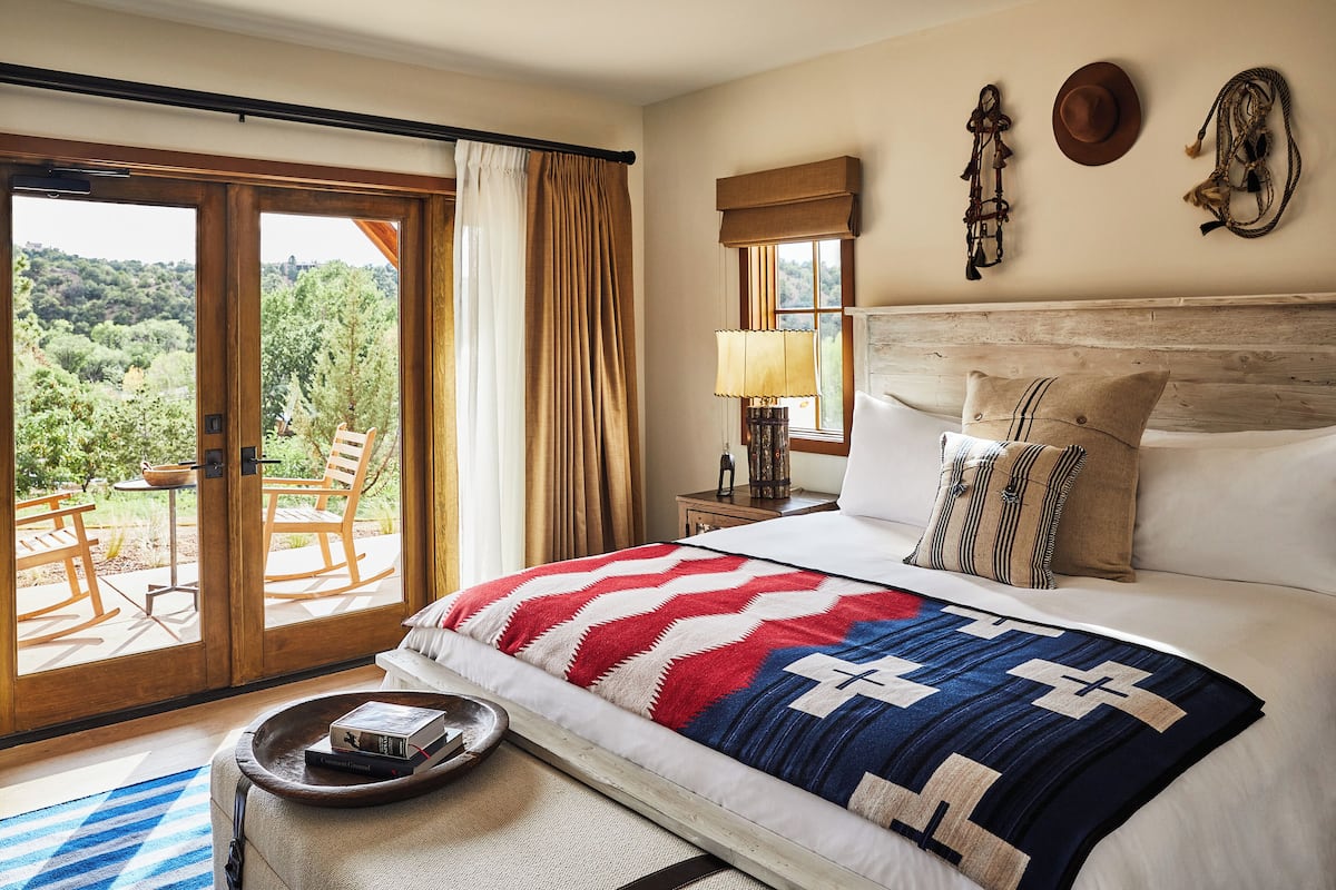 A bedroom with a large bed, a view of the outdoors, a wooden headboard, and a nightstand with a lamp.