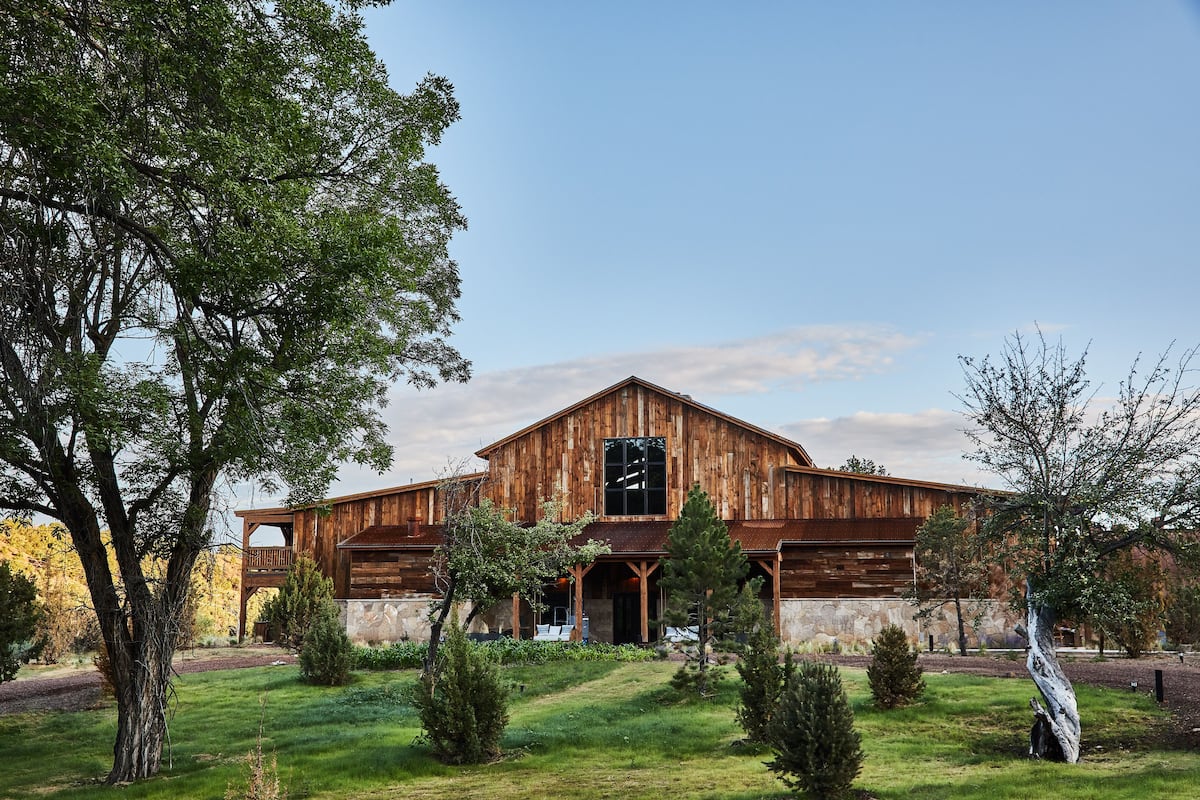 A rustic wooden building with a large window and a balcony, surrounded by a well-maintained lawn and trees.