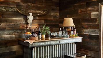 A rustic bar area with a wooden wall, a skull decoration, and various bottles and fruits on the counter.