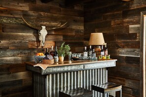 A rustic bar area with a wooden wall, a skull decoration, and various bottles and fruits on the counter.