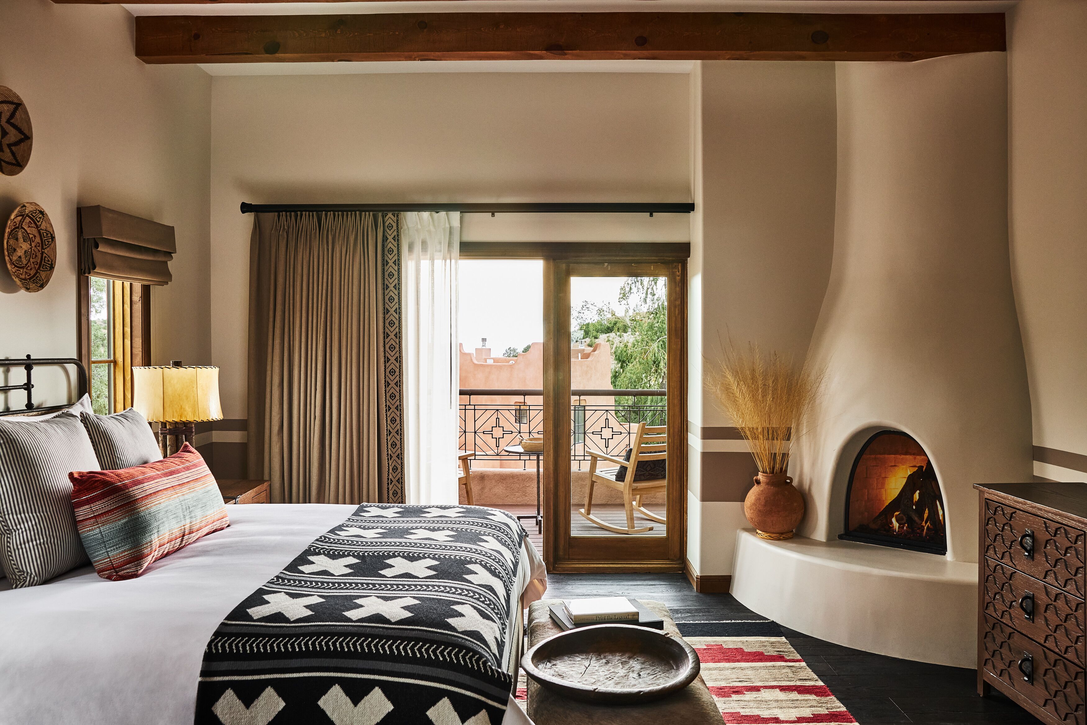 A bedroom with a bed, a fireplace, a balcony, and a view of the outside.