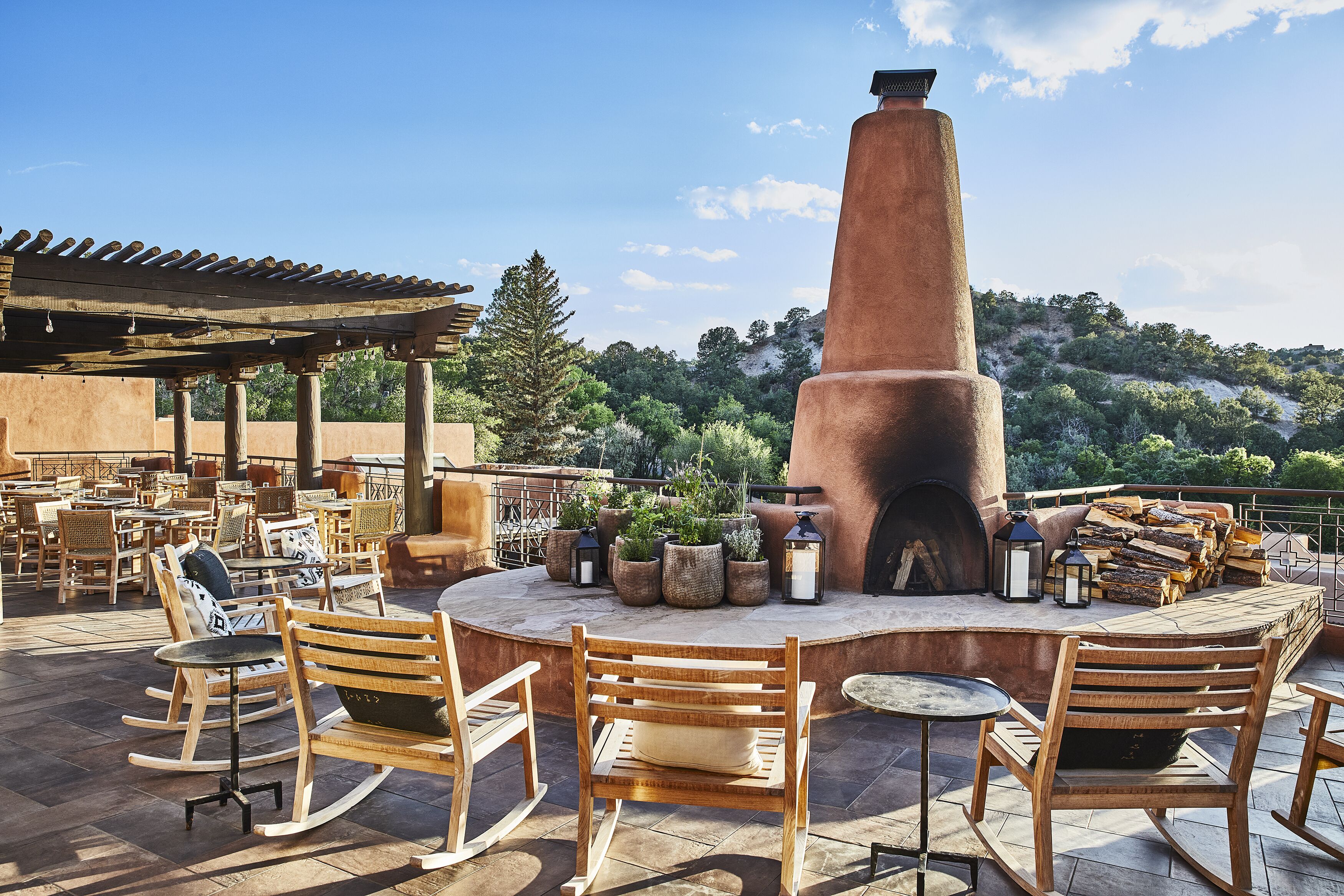 An outdoor patio with wooden rocking chairs, a central fire pit, and potted plants.