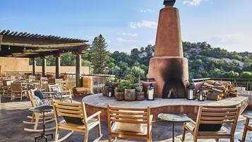 An outdoor patio with wooden rocking chairs, a central fire pit, and potted plants.