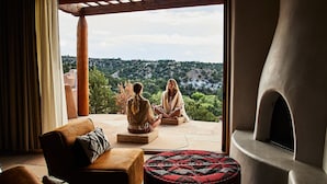 A room with a view of a hillside, a fireplace, and two people sitting on cushions. - Bishop's Lodge, Auberge Collection (Santa Fe)