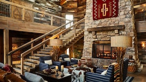 A cozy interior with a stone fireplace, a wooden staircase, and a seating area with blue upholstered chairs and a leather couch. - Bishop's Lodge, Auberge Collection (Santa Fe)