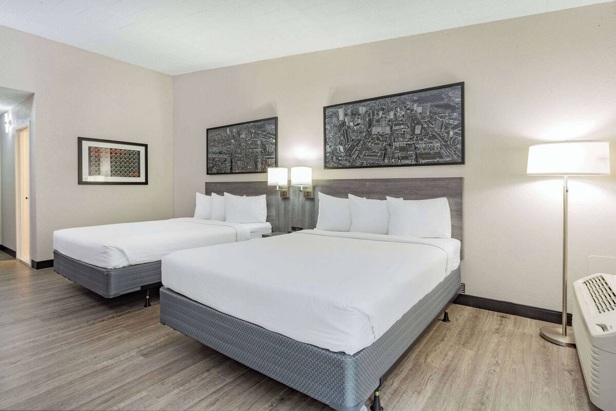 A hotel room with two beds, a cityscape artwork on the wall, and a standing lamp.