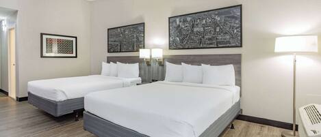 A hotel room with two beds, a cityscape artwork on the wall, and a standing lamp.