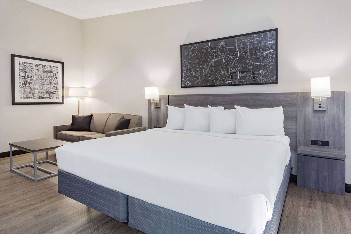 A hotel room with a large bed, a desk, a chair, and two wall-mounted lamps.