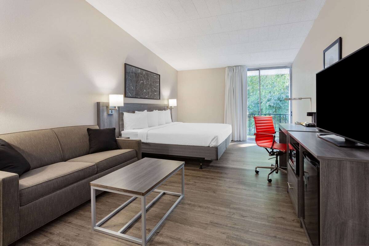 A hotel room with a bed, a sofa, a coffee table, a TV, and a desk.