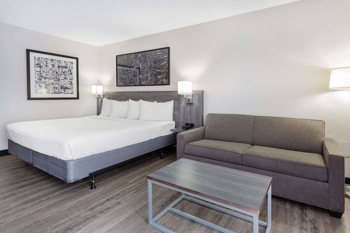 A hotel room with a bed, a sofa, a coffee table, and two wall-mounted lamps.
