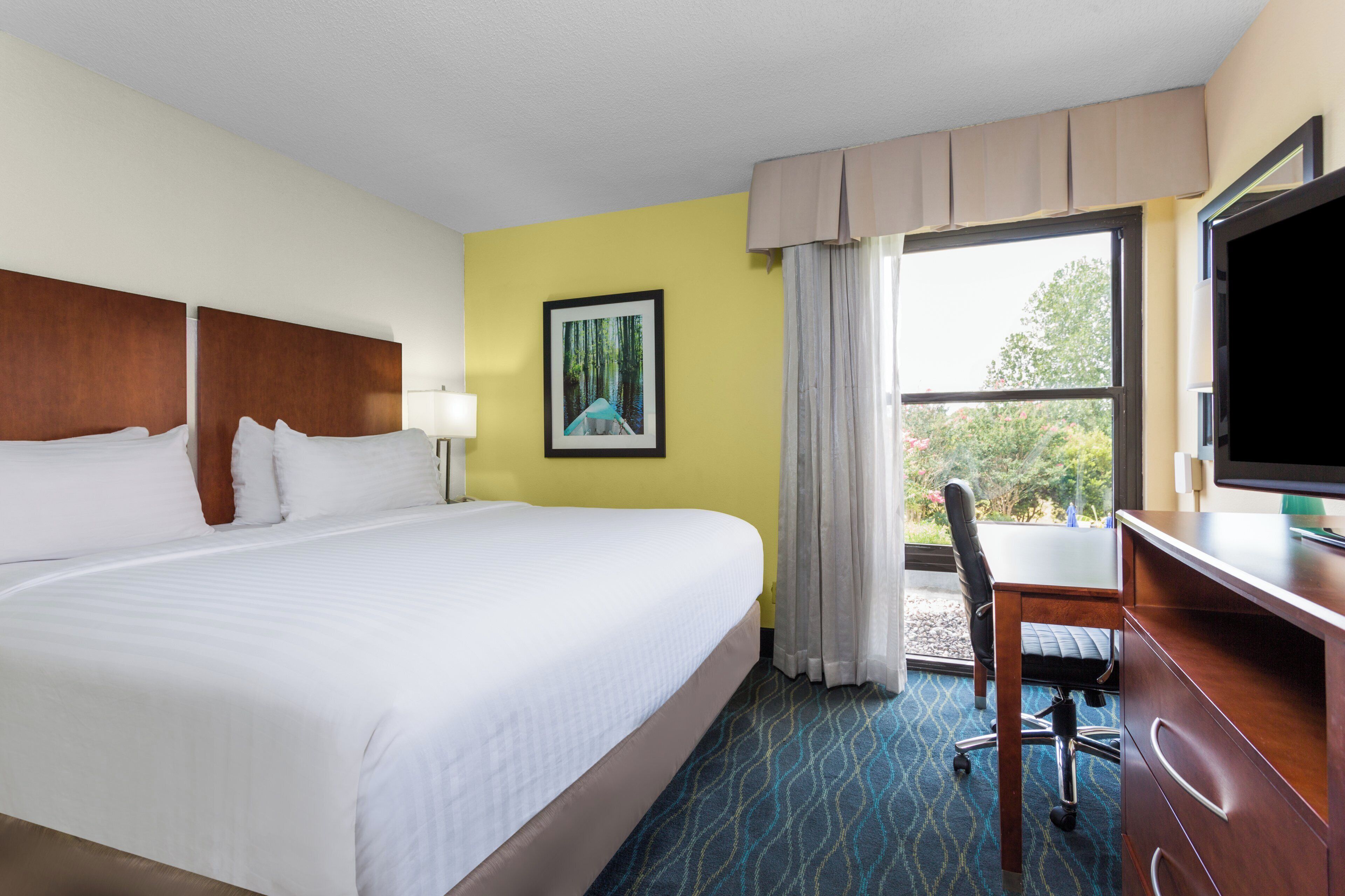 A hotel room with a large bed, a desk with a chair, a television, and a window with curtains.