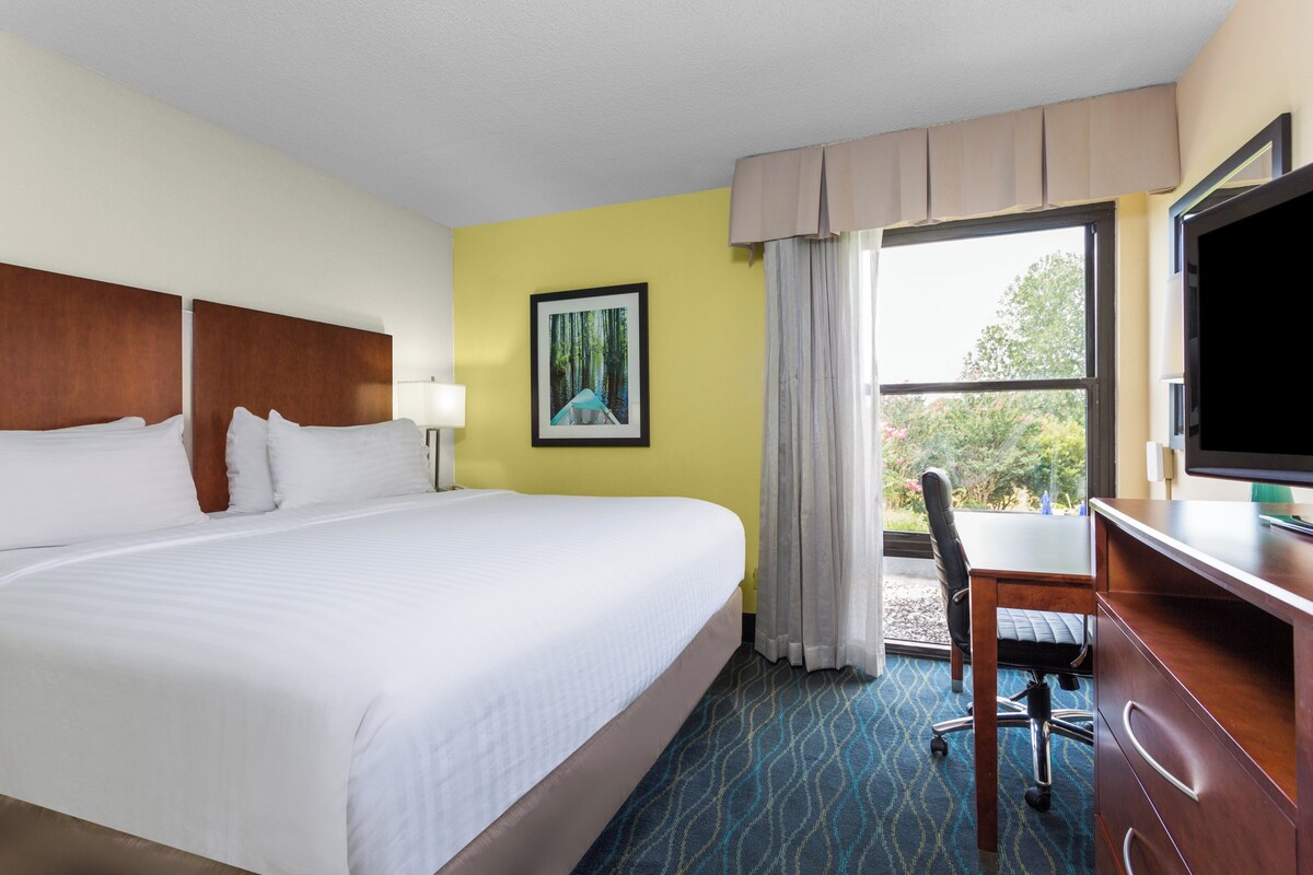 A hotel room with a large bed, a desk with a chair, a television, and a window with curtains.