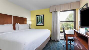 A hotel room with a large bed, a desk with a chair, a television, and a window with curtains.