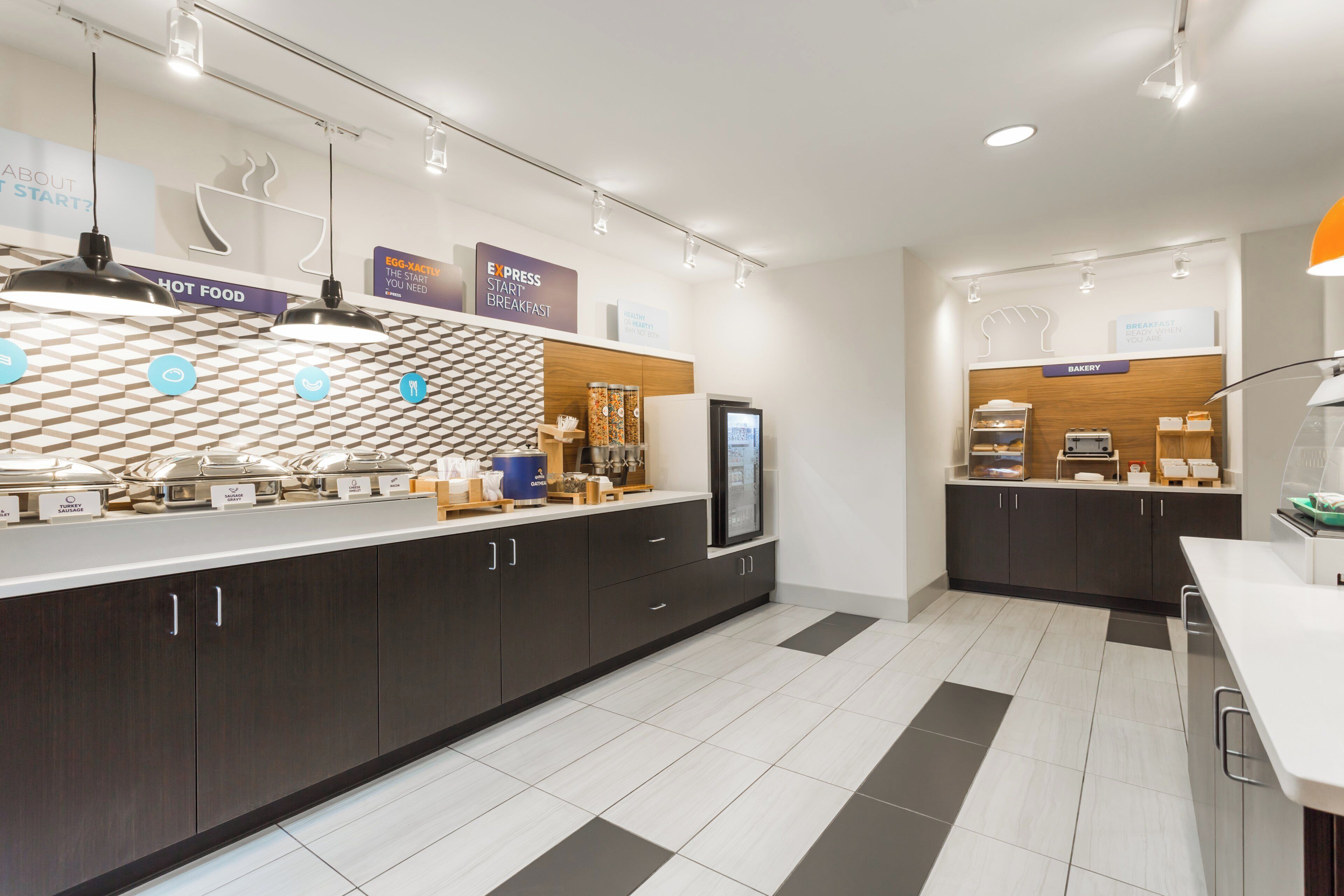 Un espace moderne dédié au petit-déjeuner, avec un comptoir en libre-service, une machine à café et un rayon de produits de boulangerie.