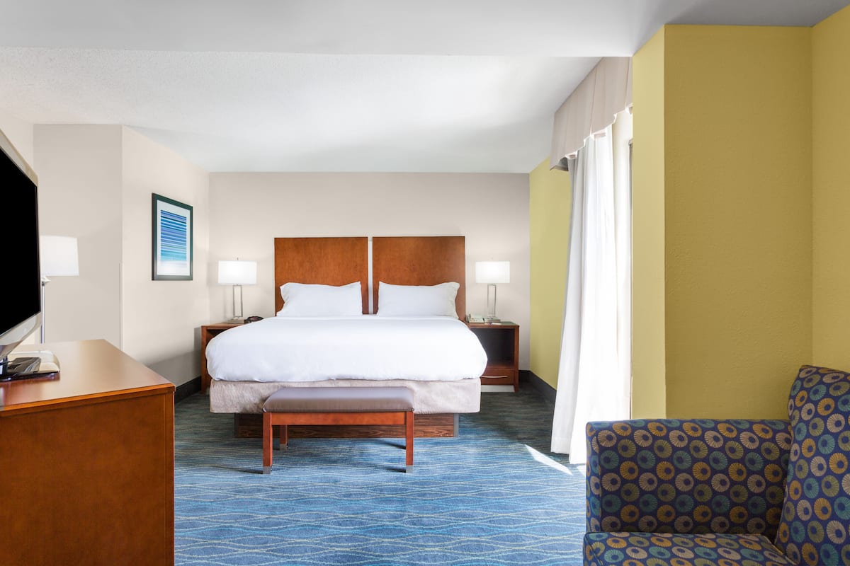 A hotel room with a large bed, bedside tables, a desk, and a patterned armchair.