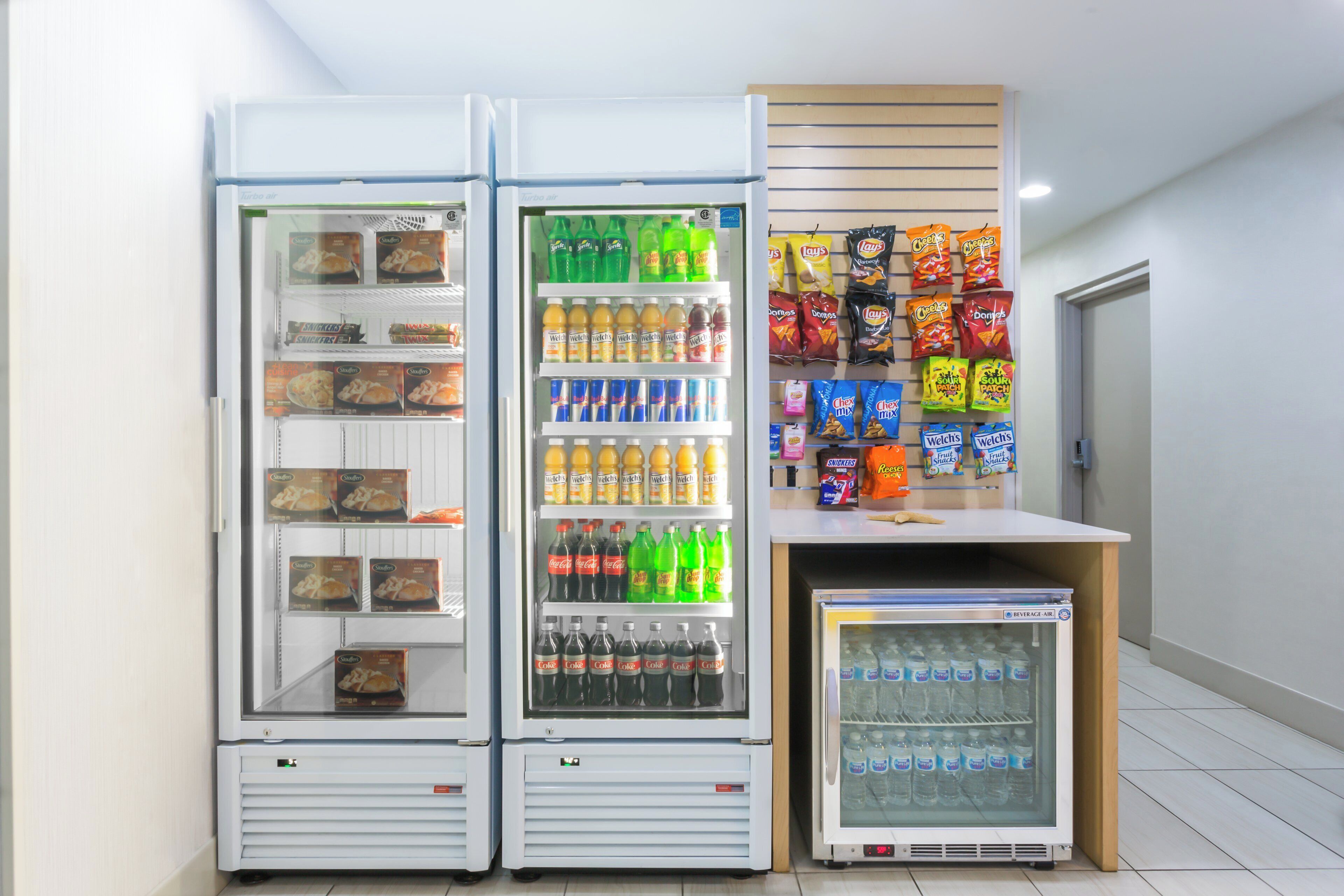 A row of beverage refrigerators stocked with various drinks and snacks.