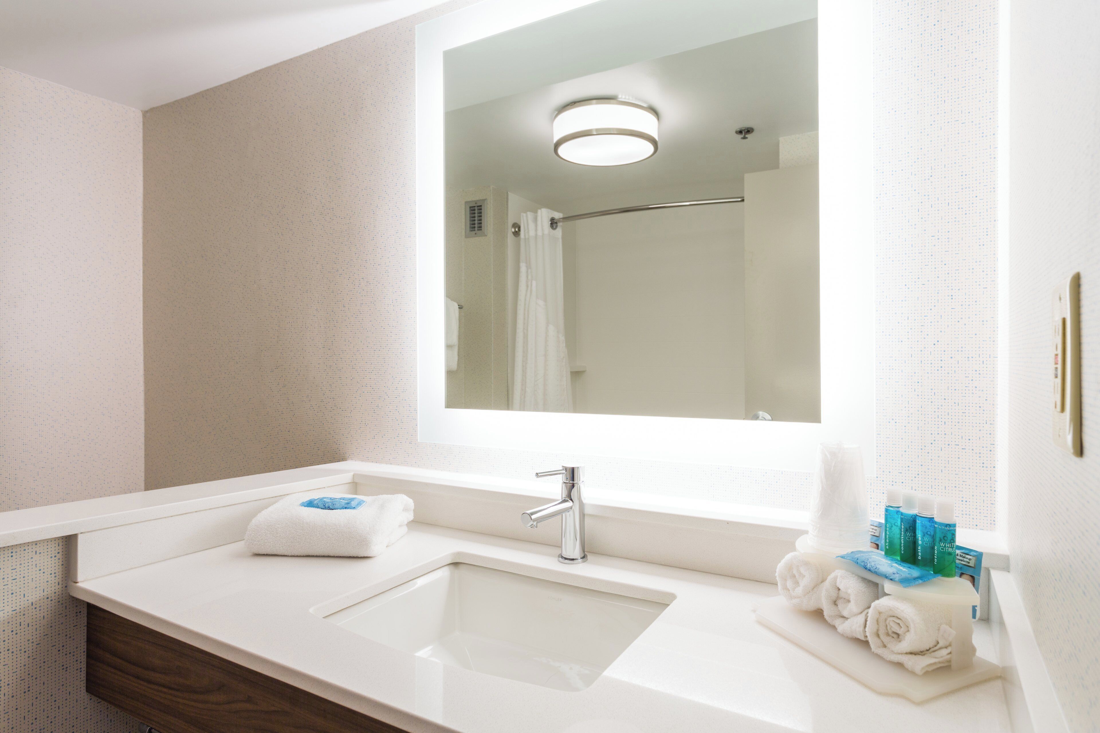 A bathroom with a white sink, a mirror, and a shower visible in the reflection.