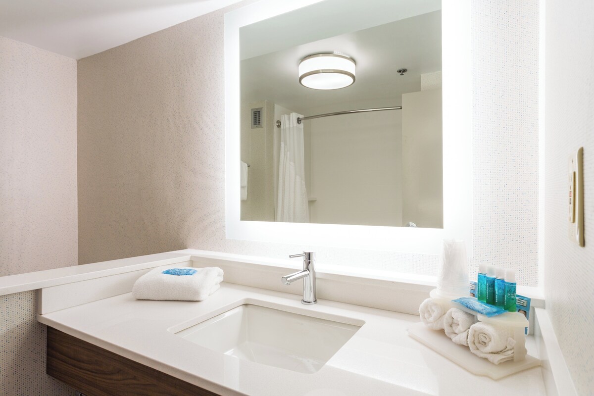 A bathroom with a white sink, a mirror, and a shower visible in the reflection.