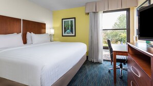 Habitación de hotel con una cama grande, un escritorio con silla, televisión y ventana con vista a árboles.