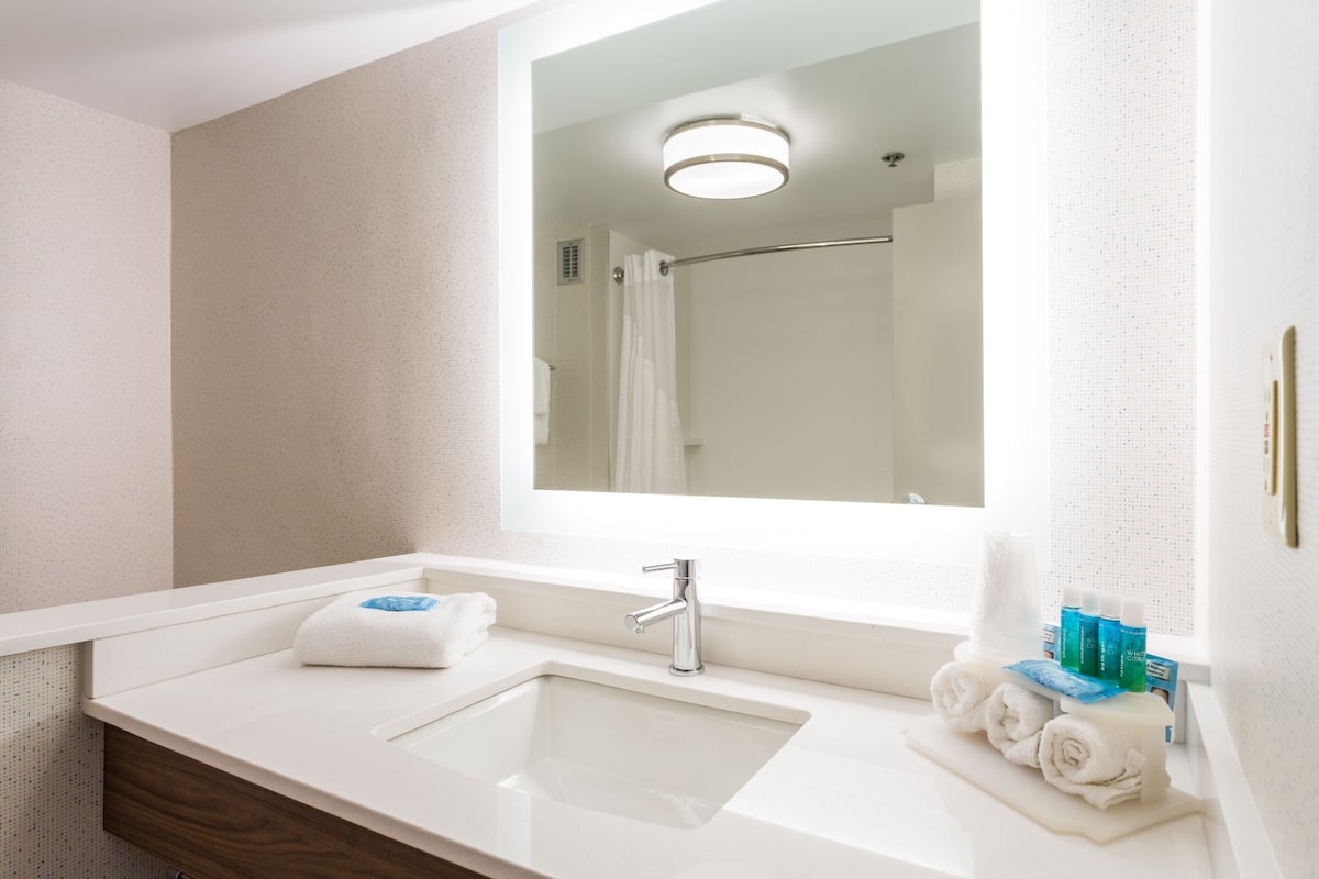 A modern bathroom with a large mirror, a sink, and a shower area.