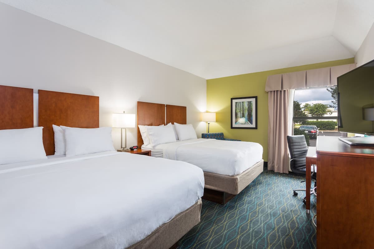 A hotel room with two beds, a desk, a chair, and a window with curtains.