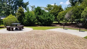 A paved outdoor area with a circular stone table and benches, surrounded by greenery and trees. - Holiday Inn Express Hotel & Suites Wilmington-University Ctr by IHG (Wilmington)