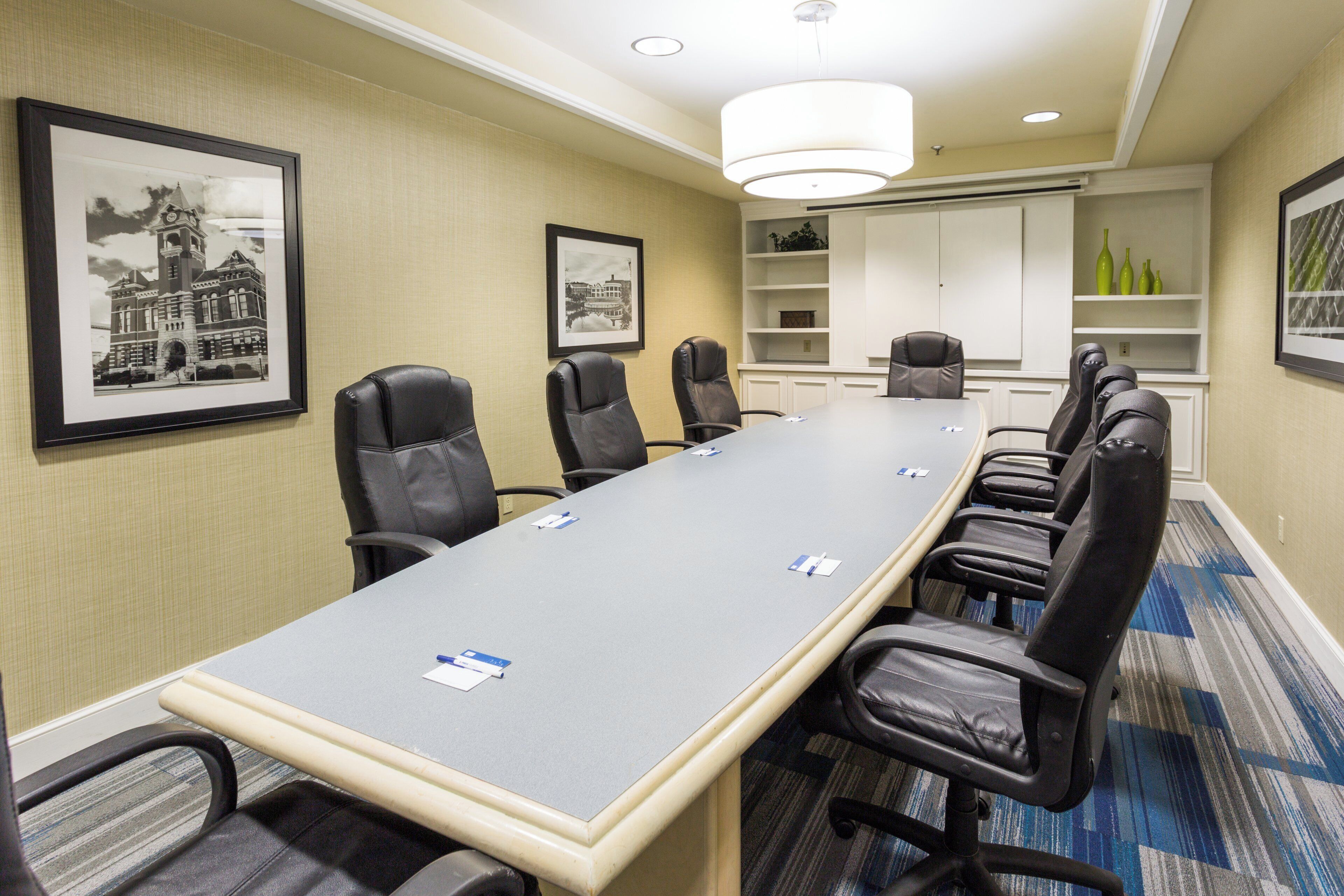 A conference room with a long table, multiple chairs, framed pictures on the walls, and a carpeted floor.